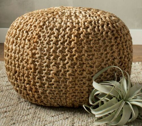 A hand knitted braided ottoman pouffe footstool made of beige jute, placed on a floor with a plant beside it.